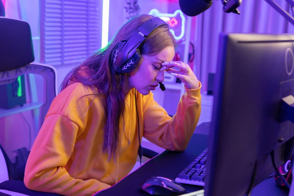A motion sick gamer holds her head in her hands and looks away from the screen, in obvious discomfort